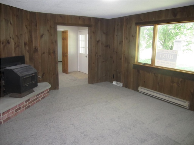 unfurnished living room featuring a wood stove, light colored carpet, baseboard heating, and a healthy amount of sunlight