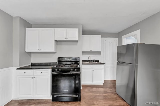 kitchen featuring white cabinets, dark wood-type flooring, sink, black gas stove, and stainless steel refrigerator