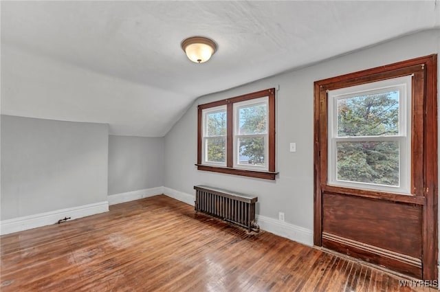 additional living space with radiator, plenty of natural light, hardwood / wood-style floors, and lofted ceiling