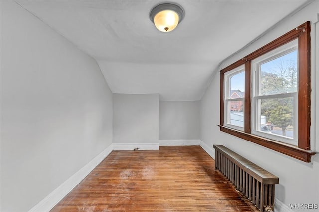 additional living space with wood-type flooring, radiator heating unit, and vaulted ceiling