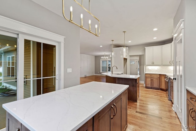 kitchen featuring light stone counters, an island with sink, sink, decorative light fixtures, and light hardwood / wood-style flooring