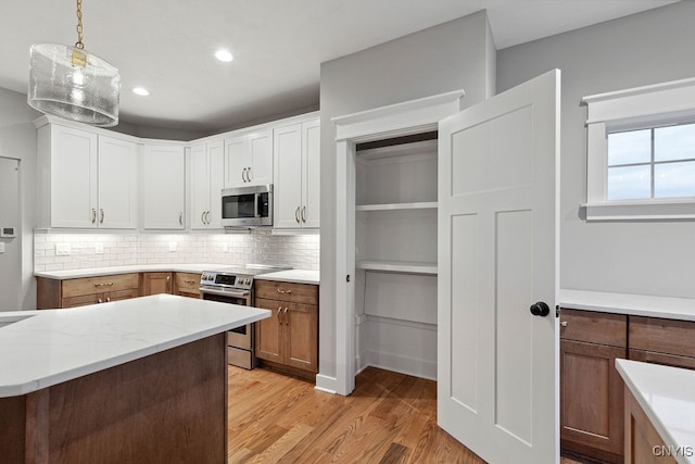 kitchen featuring decorative light fixtures, backsplash, light hardwood / wood-style flooring, white cabinetry, and appliances with stainless steel finishes