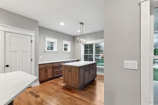 kitchen with light wood-type flooring, an inviting chandelier, a center island, and decorative light fixtures