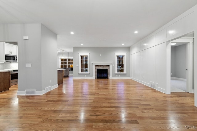 unfurnished living room featuring a stone fireplace and light hardwood / wood-style floors