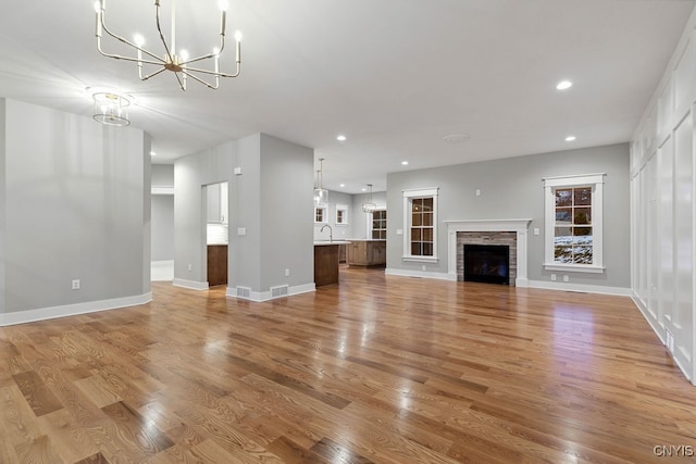 unfurnished living room featuring an inviting chandelier, light wood-type flooring, and a stone fireplace