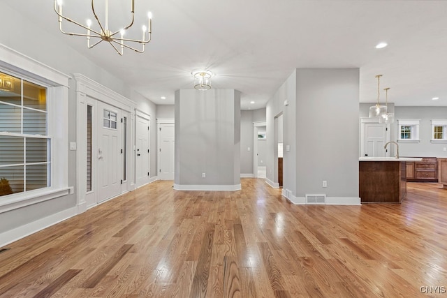 unfurnished living room featuring a notable chandelier and light wood-type flooring