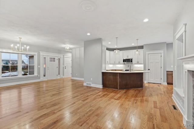 kitchen with pendant lighting, light wood-type flooring, a notable chandelier, white cabinetry, and backsplash