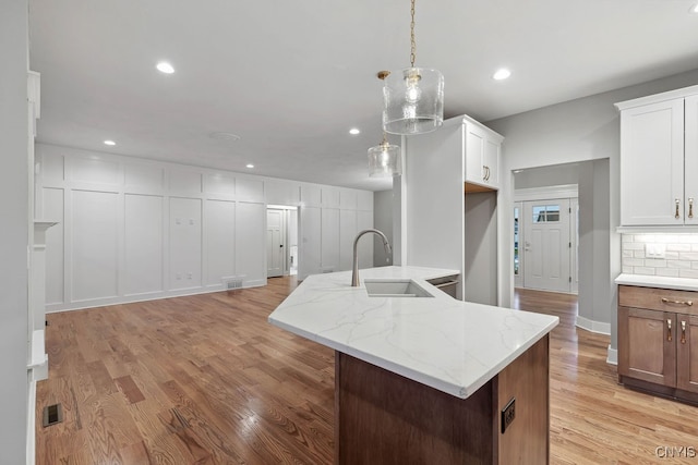 kitchen featuring white cabinetry, an island with sink, light hardwood / wood-style flooring, decorative light fixtures, and sink