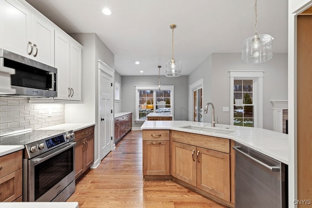 kitchen featuring light hardwood / wood-style floors, sink, white cabinets, hanging light fixtures, and stainless steel appliances