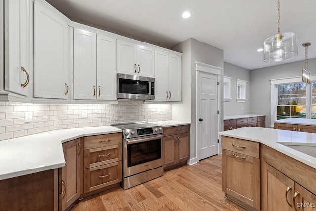 kitchen featuring appliances with stainless steel finishes, hanging light fixtures, light hardwood / wood-style floors, and white cabinets