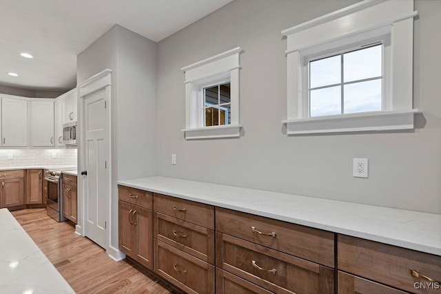 kitchen featuring light wood-type flooring, white cabinets, decorative backsplash, stainless steel appliances, and light stone countertops