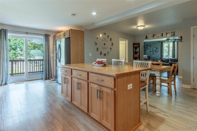 kitchen with wood counters, stainless steel fridge, light wood-type flooring, a center island, and a breakfast bar area