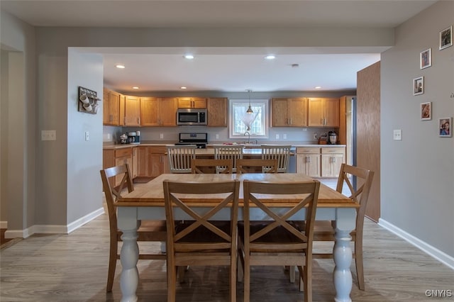 kitchen featuring appliances with stainless steel finishes, light hardwood / wood-style flooring, hanging light fixtures, and sink