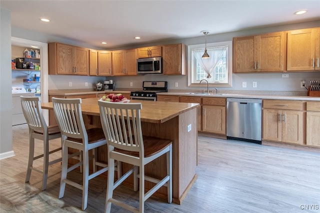 kitchen featuring sink, light hardwood / wood-style flooring, independent washer and dryer, decorative light fixtures, and stainless steel appliances