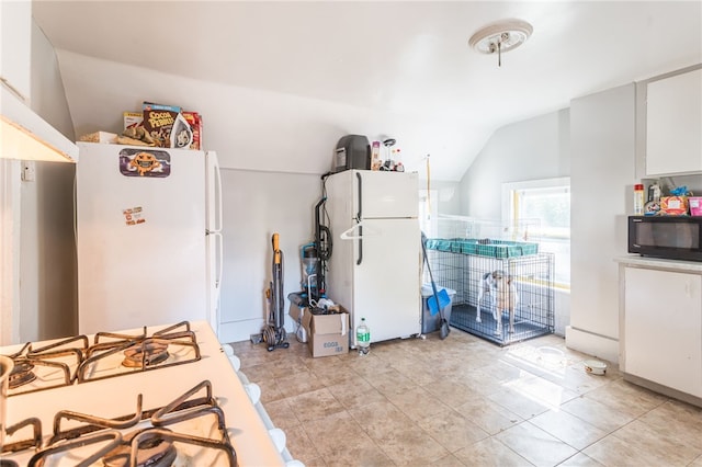 kitchen featuring white cabinets, lofted ceiling, light tile patterned floors, and white fridge