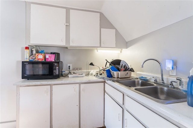 kitchen with lofted ceiling, white cabinetry, and sink