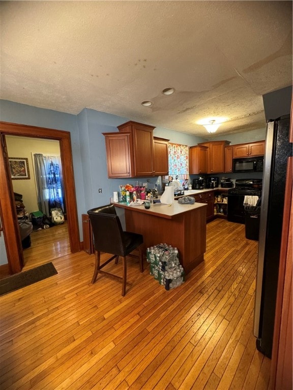 kitchen featuring light wood-type flooring, a textured ceiling, kitchen peninsula, a kitchen breakfast bar, and black appliances