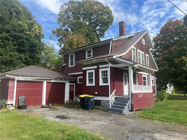 view of front facade with a front yard, a garage, covered porch, and an outbuilding