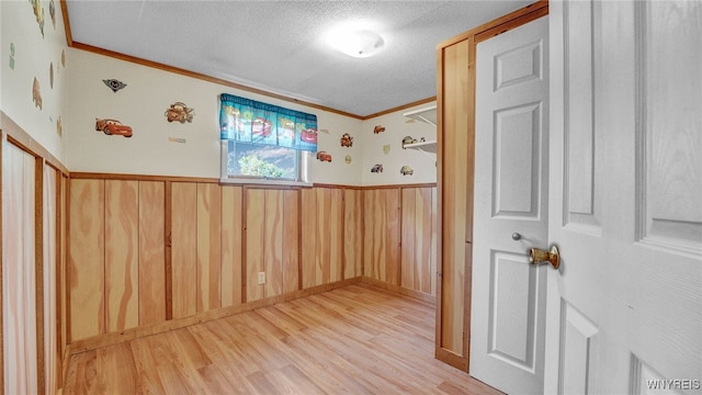 unfurnished room featuring a textured ceiling, wood walls, light hardwood / wood-style floors, and crown molding