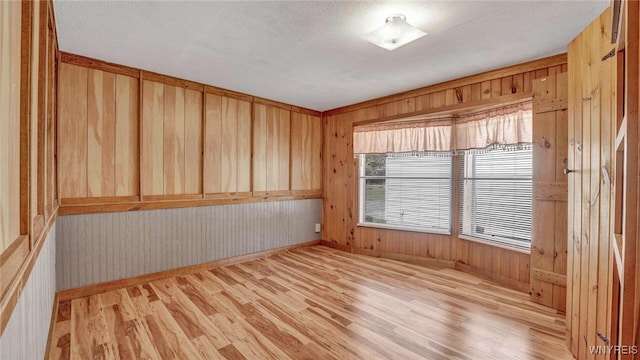 spare room with a textured ceiling, light hardwood / wood-style floors, and wooden walls