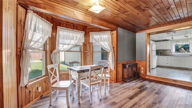 dining space featuring wooden walls, light wood-type flooring, sink, and wood ceiling