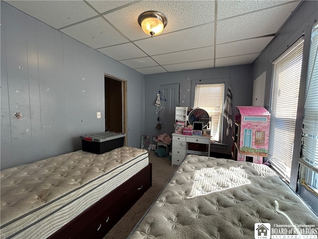 carpeted bedroom with wood walls and a paneled ceiling