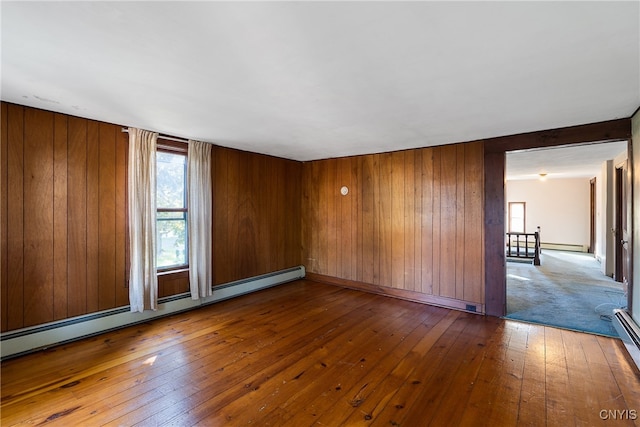 unfurnished room featuring wood-type flooring, wood walls, and baseboard heating