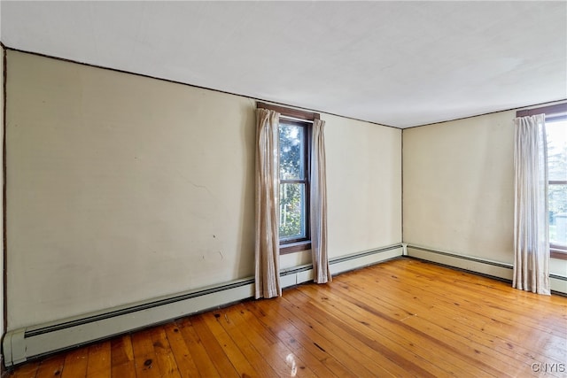 unfurnished room with a baseboard heating unit, a wealth of natural light, and light hardwood / wood-style floors