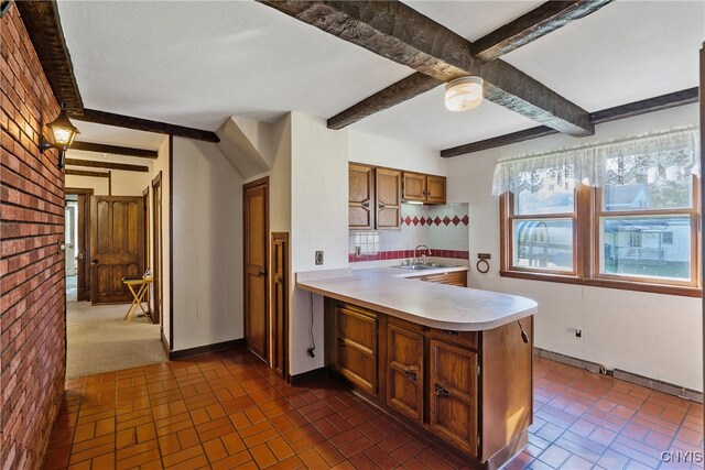 kitchen featuring sink, beam ceiling, kitchen peninsula, brick wall, and backsplash