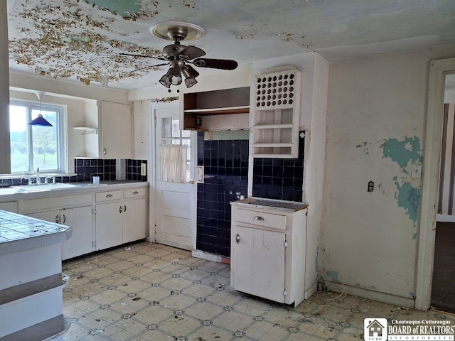 kitchen with ceiling fan, white cabinets, sink, and tile counters