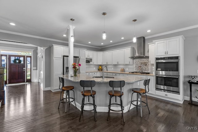 kitchen with appliances with stainless steel finishes, wall chimney exhaust hood, white cabinets, and decorative light fixtures