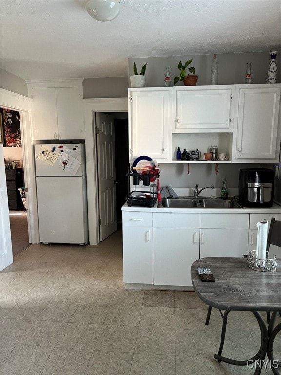 kitchen featuring a textured ceiling, white cabinetry, white refrigerator, and sink