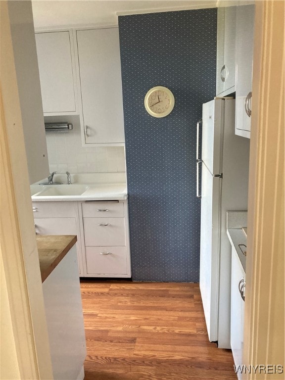 kitchen with white cabinets, sink, light wood-type flooring, and white fridge