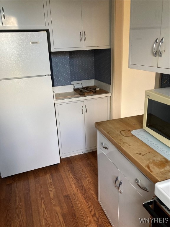 kitchen featuring dark wood-type flooring, stove, white fridge, and tasteful backsplash