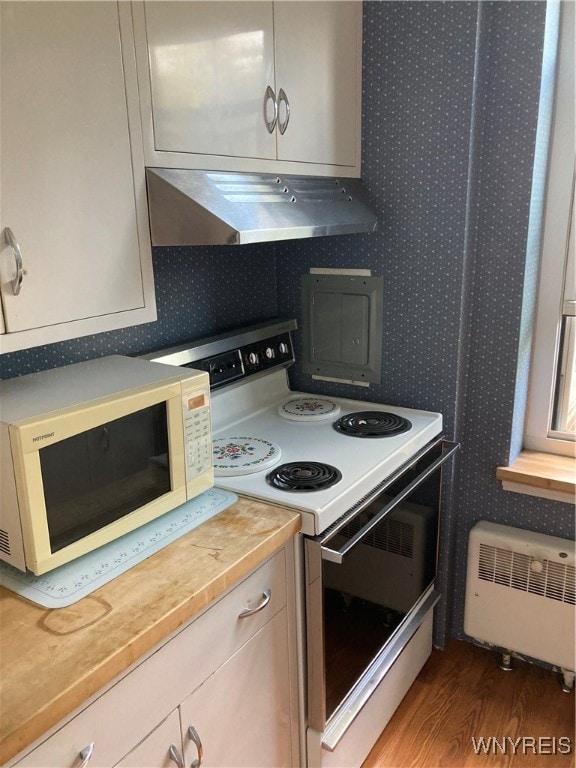 kitchen featuring radiator heating unit, wooden counters, white appliances, hardwood / wood-style flooring, and range hood