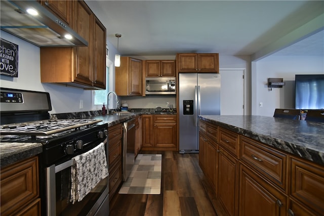 kitchen with hanging light fixtures, extractor fan, stainless steel appliances, dark stone counters, and dark hardwood / wood-style flooring