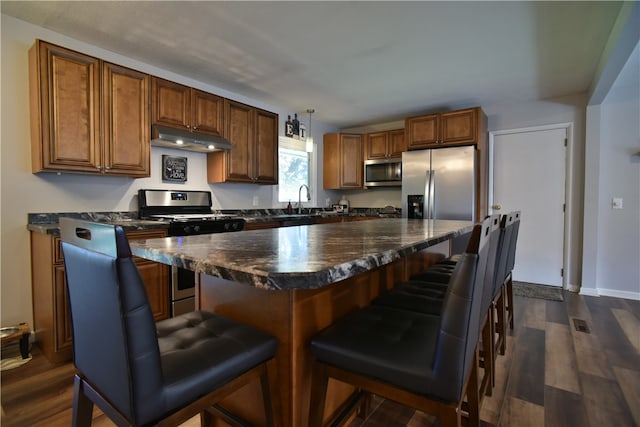 kitchen with appliances with stainless steel finishes, a kitchen island, a kitchen bar, dark hardwood / wood-style floors, and sink