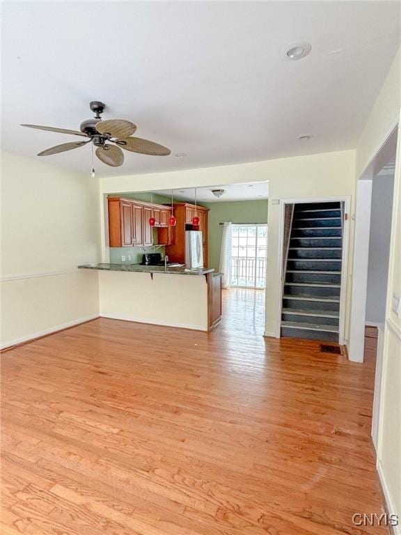 interior space with kitchen peninsula, a kitchen breakfast bar, ceiling fan, light hardwood / wood-style flooring, and white fridge