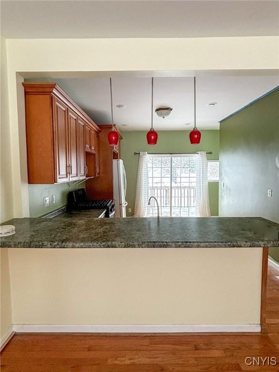 kitchen with white refrigerator, black stove, kitchen peninsula, hanging light fixtures, and wood-type flooring