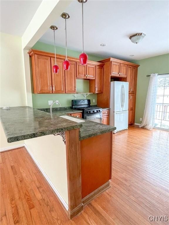 kitchen with gas stove, kitchen peninsula, white fridge, pendant lighting, and light hardwood / wood-style floors