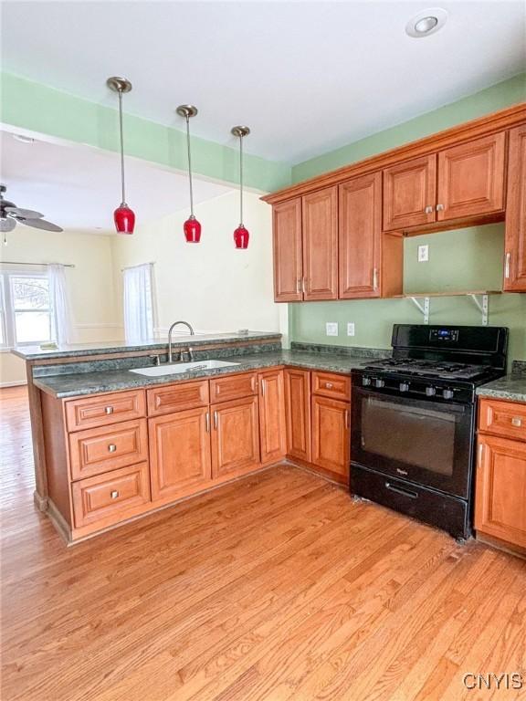 kitchen with gas stove, ceiling fan, sink, hanging light fixtures, and light wood-type flooring