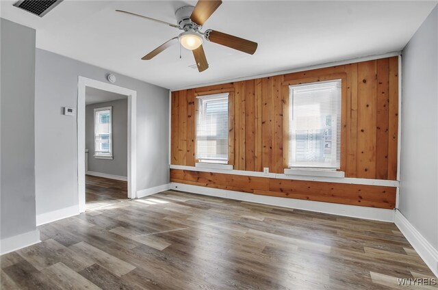 empty room featuring wood-type flooring, wood walls, and ceiling fan