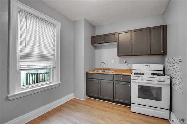 kitchen with light hardwood / wood-style flooring, a wealth of natural light, white gas stove, and sink