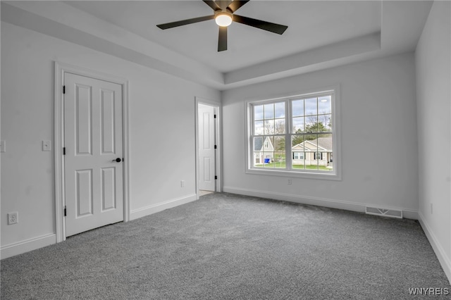 unfurnished room with a tray ceiling, ceiling fan, and carpet