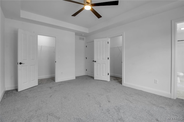 unfurnished bedroom with a raised ceiling, ensuite bathroom, ceiling fan, and light carpet