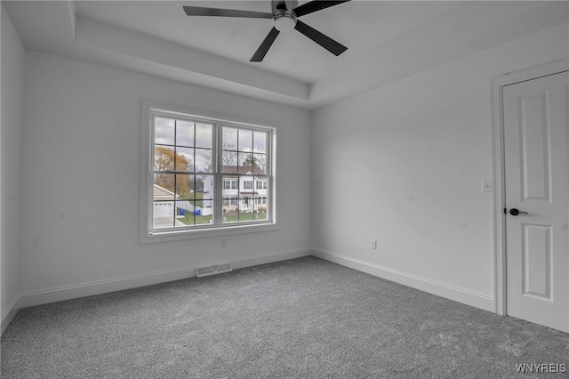 carpeted spare room with a raised ceiling and ceiling fan