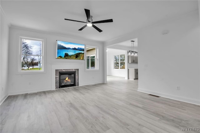 unfurnished living room featuring ceiling fan, a healthy amount of sunlight, light hardwood / wood-style floors, and a tiled fireplace