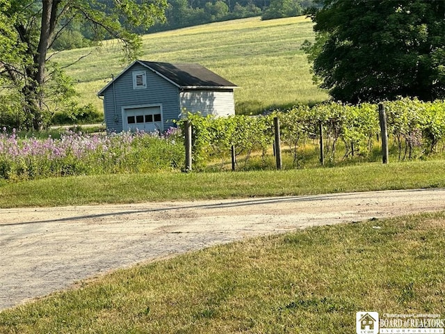 view of property exterior featuring a detached garage, an outbuilding, and a rural view