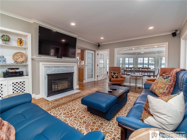 living room featuring built in features, wood finished floors, ornamental molding, and a fireplace with flush hearth