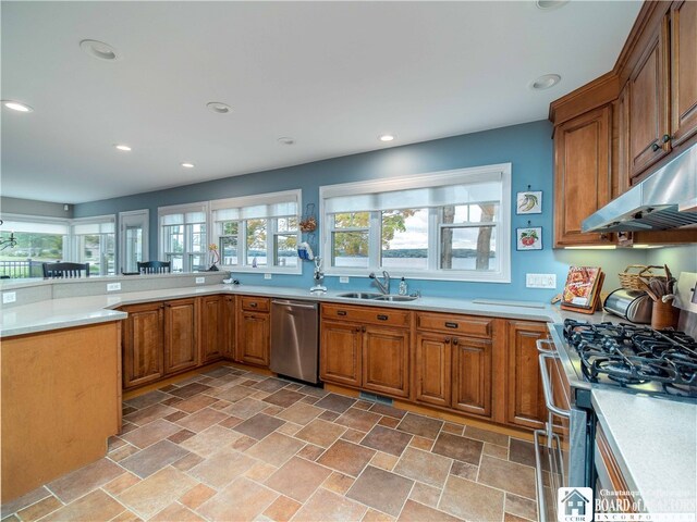 kitchen with a sink, stainless steel appliances, light countertops, under cabinet range hood, and brown cabinets